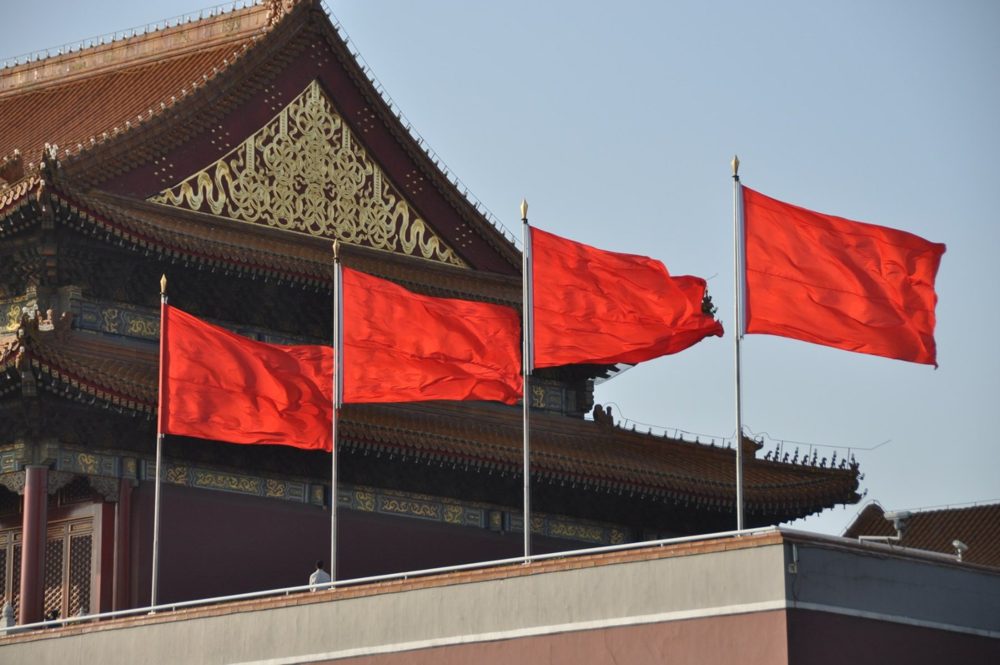 Red flags flying along the top of the Gate of Heavenly Peace, beneath its golden roof and painted eaves.