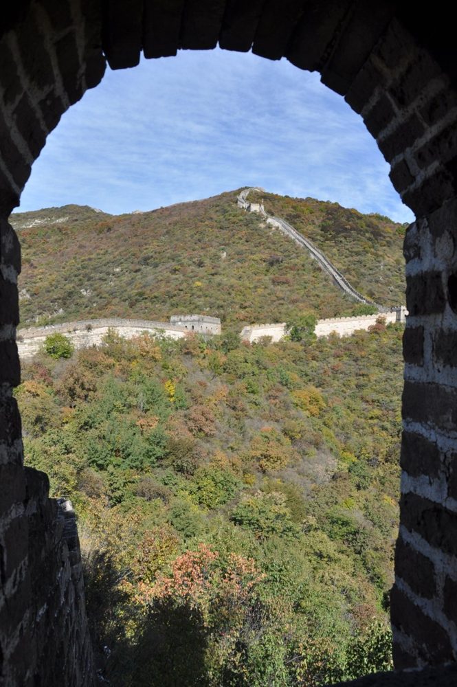A view through an arched watchtower window on the Great Wall, looking out at the wall climbing the next ridge.