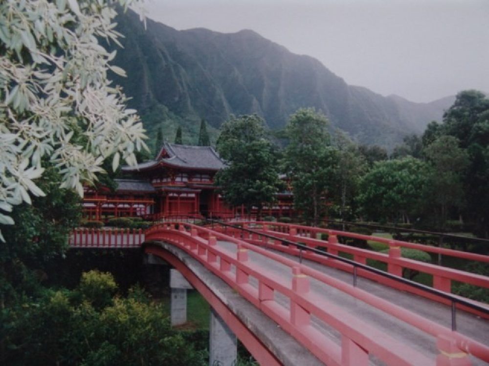 A red arched bridge in the gardens of the Byodo-In Temple, with clouds resting on the Koʻolau cliffs above.