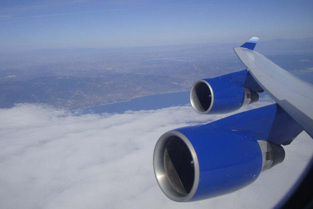 A four-engine wide-body in cruise, the coastline below the cloud.