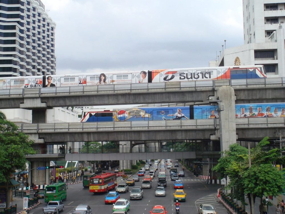 A BTS Skytrain passes along an elevated track above busy traffic in central Bangkok.