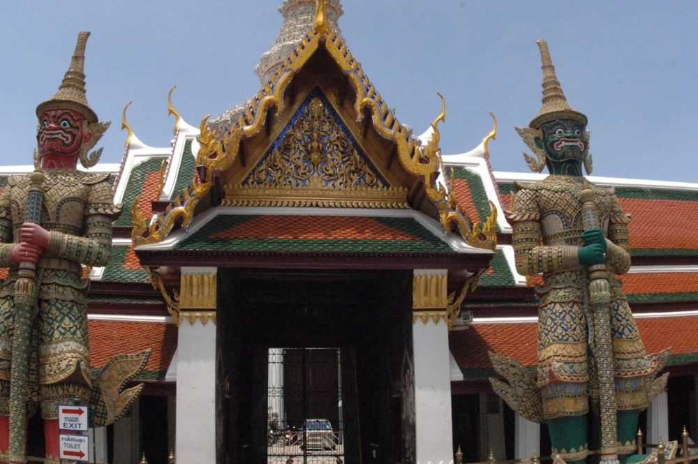Two giant yaksha guardian statues, one red-faced and one green-faced, flanking a gateway at Wat Phra Kaew, Bangkok.