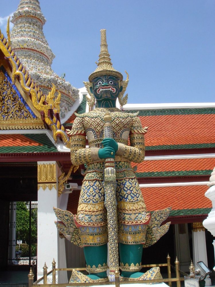 A green-faced yaksha guardian statue standing with a tall club before a temple building at Wat Phra Kaew, Bangkok.