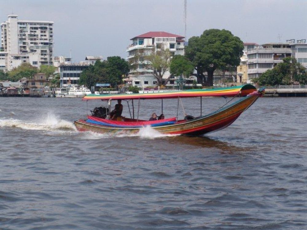 A long-tail boat with a striped canopy speeding across the Chao Phraya River, Bangkok.